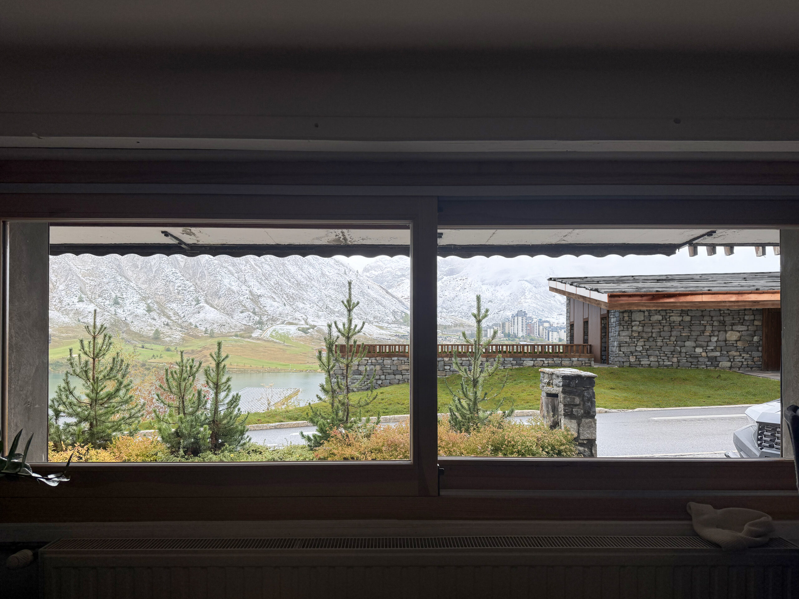 Visualisation depuis l'intérieur du chalet, cadrant les montagnes à travers la baie vitrée, soulignant la connexion visuelle de l'insertion paysagère chalet.